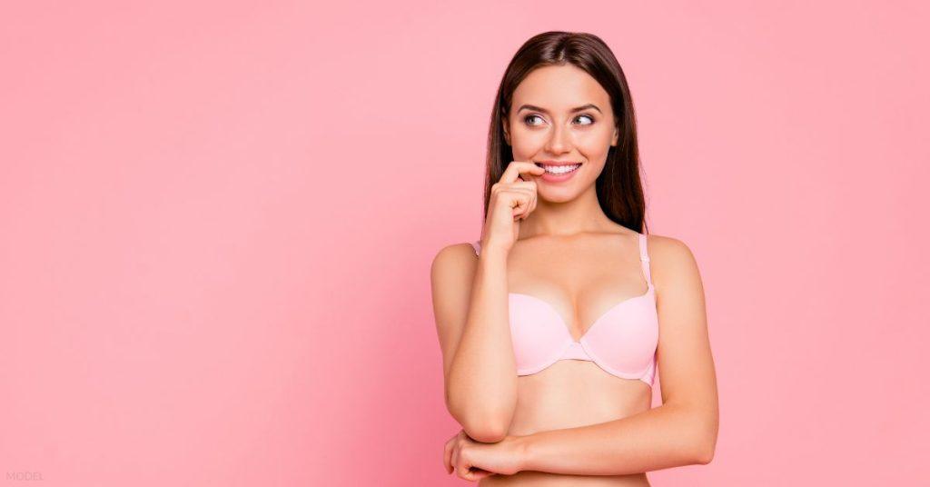 Girl with hand near mouth in pink underwear isolated on pink background. (MODEL)