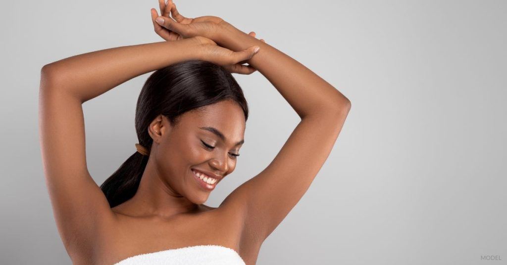 Woman wrapped in a towel, arms raised and hands resting on her head. (MODEL)